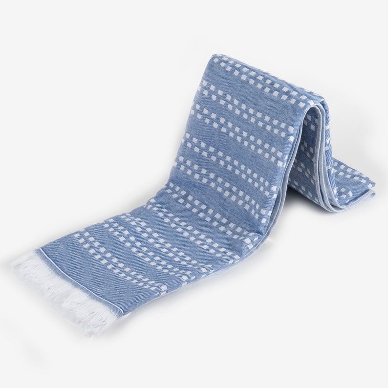 May include: A blue and white patterned towel with fringe. The towel is folded in half and has a white background with blue squares.