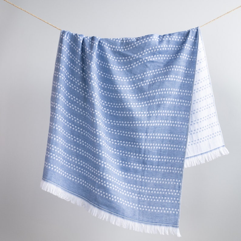 May include: A blue and white striped beach towel with a fringe border. The towel is hanging on a clothesline.
