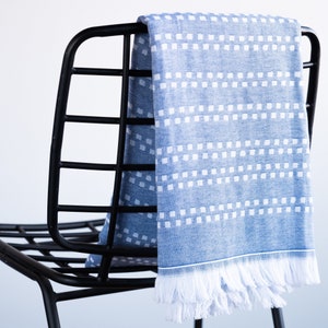 May include: A blue and white patterned throw blanket with a fringe border draped over a black metal chair.
