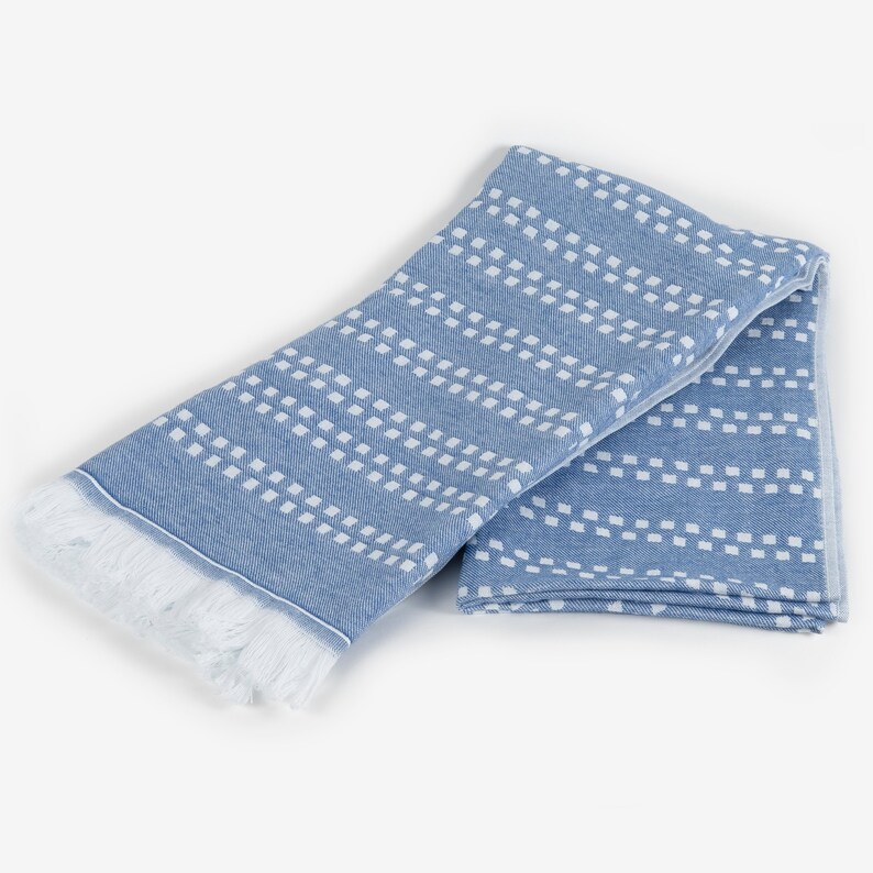 May include: A blue and white patterned towel with a fringe border. The towel is folded in half and has a geometric design.