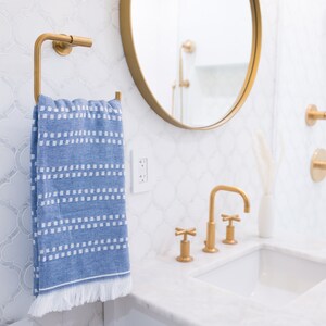 May include: A white bathroom sink with gold faucets and a blue and white striped towel hanging on a gold towel rack.