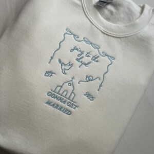 May include: White sweatshirt with blue embroidered text that reads "going to the chapel gonna get married" with a church, dove, and hearts.