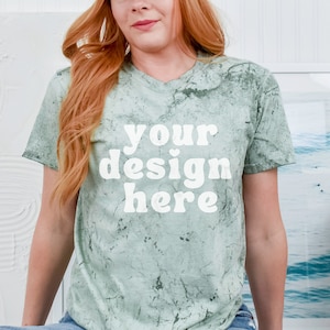 May include: A woman wearing a green tie-dye t-shirt with the text "your design here" in white. She is wearing blue jeans with a distressed look.