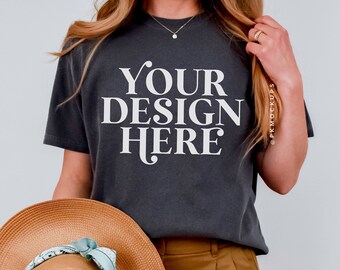 May include: A dark gray t-shirt with the text "YOUR DESIGN HERE" printed on the front. The t-shirt is being worn by a person wearing brown shorts and a straw hat.