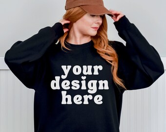 May include: A black sweatshirt with the text "your design here" in white. The sweatshirt is being modelled by a person with long red hair wearing a brown baseball cap.