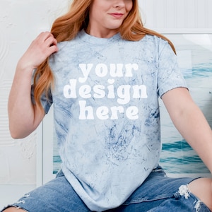 May include: A light blue tie-dye t-shirt with the text "your design here" in white. The shirt is being worn by a person with long red hair.