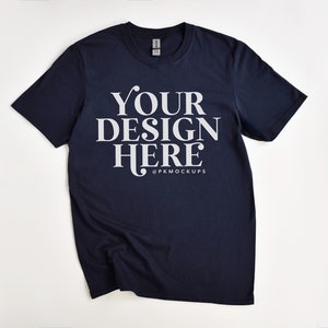 May include: A navy blue t-shirt with the text "YOUR DESIGN HERE" in white lettering. The text is centered on the shirt and is surrounded by a white border. The shirt is lying flat on a white surface.