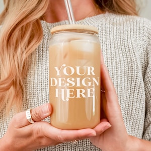 May include: A person holding a clear glass tumbler with a wooden lid and a straw. The tumbler is filled with a light brown beverage and ice. The text "YOUR DESIGN HERE" is printed on the side of the tumbler.