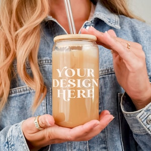 May include: A person holding a clear glass can with a bamboo lid and a straw. The can is filled with a light brown liquid and has the text "YOUR DESIGN HERE" printed on it.