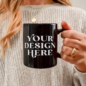 Puede incluir: Una taza de cerámica negra con asa blanca. La taza tiene el texto "YOUR DESIGN HERE" impreso en la parte delantera.
