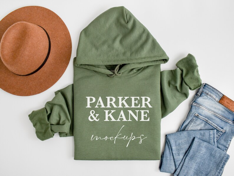 May include: A green hooded sweatshirt with the text "PARKER & KANE mockups" printed on the front. The sweatshirt is laid flat on a white surface with a brown hat and blue jeans.