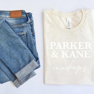 May include: A folded pair of blue jeans and a folded cream colored t-shirt with the text "Parker & Kane mockups" printed in white.