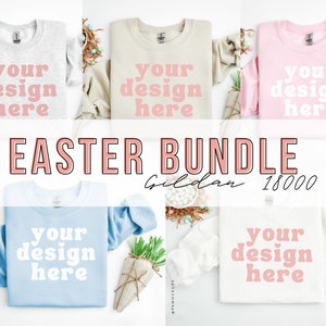 Op de afbeelding: Een set van vijf Gildan 18000 crewneck sweatshirts in verschillende kleuren, waaronder grijs, beige, roze, lichtblauw en wit. Elk sweatshirt heeft de tekst "your design here" in roze letters.