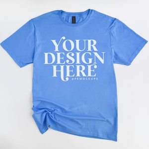 May include: A light blue t-shirt with the text "YOUR DESIGN HERE" in white lettering. The shirt is laid flat on a white background.