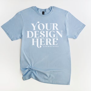 May include: A light blue t-shirt with the text "YOUR DESIGN HERE" and the social media handle "@PKMOCKUPS" printed on the front.