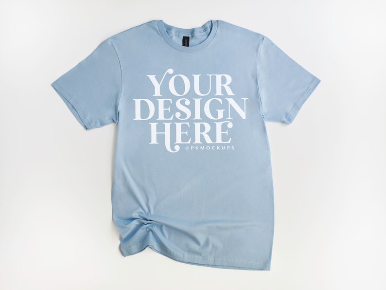 May include: A light blue t-shirt with the text "YOUR DESIGN HERE" and the social media handle "@PKMOCKUPS" printed on the front.