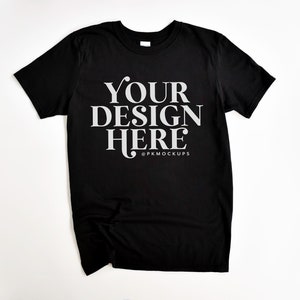 May include: Black t-shirt with the text "YOUR DESIGN HERE" in white lettering and the text "@PKMOCKUPS" in smaller white lettering below.