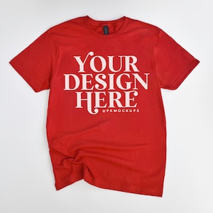Puede incluir: Camiseta roja con el texto "YOUR DESIGN HERE" en letras blancas. La camiseta está arrugada y puesta plana sobre una superficie blanca.