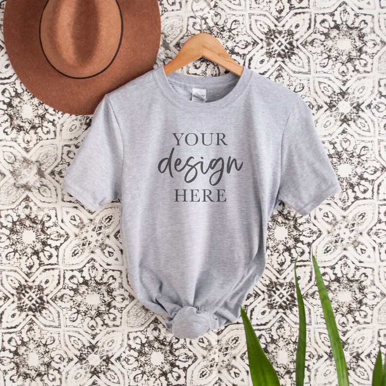 Op de afbeelding: Een grijs T-shirt met korte mouwen hangend aan een houten hanger. Op het T-shirt staat de tekst "YOUR design HERE" gedrukt.