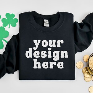 May include: Black sweatshirt with the text "your design here" in white. The image includes green shamrock cutouts and a bowl of gold coins, suggesting a St. Patrick's Day theme.