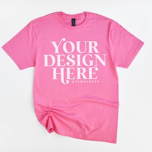 Könnte beinhalten: Pinkes T-Shirt mit dem Text "YOUR DESIGN HERE" in weißen Buchstaben. Das Shirt liegt flach auf einem weißen Hintergrund.