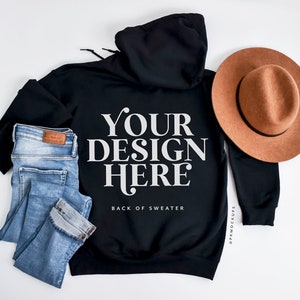 May include: Black hoodie with the text "YOUR DESIGN HERE" and the words "BACK OF SWEATER" below it. Light blue jeans and a brown hat are also in the image.