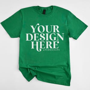 May include: A green t-shirt with the text "YOUR DESIGN HERE" in white lettering. The shirt is crumpled and laid flat on a white background.