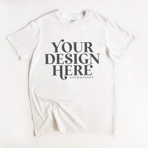 May include: White t-shirt with the text "YOUR DESIGN HERE" and the copyright symbol followed by "PKMOCKUPS".