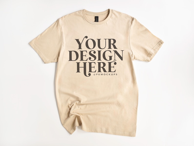 May include: A beige t-shirt with short sleeves and a crew neck. The shirt has the text "YOUR DESIGN HERE" printed on the front in black.