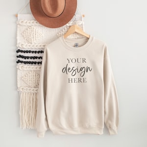 Könnte beinhalten: Ein cremefarbener Pullover mit langen Ärmeln und einem Rundhalsausschnitt. Der Pullover hat den Text "YOUR design HERE" auf der Vorderseite.