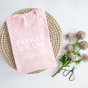 May include: A pink t-shirt with the text "PARKER & KANE mockups" printed on it. The t-shirt is folded and placed on a woven basket.