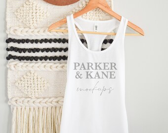May include: White tank top with a racerback design hanging on a wooden hanger. The tank top has the text "PARKER & KANE mockups" printed on the front in gray.