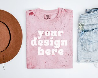 Könnte beinhalten: Pinkes T-Shirt mit einem weißen "your design here" Textüberlagerung. Das Shirt hat einen Used-Look mit weißen Flecken auf der gesamten Oberfläche. Das T-Shirt liegt flach auf einer weißen Oberfläche.