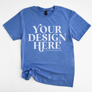 May include: A blue t-shirt with the text "YOUR DESIGN HERE" in white lettering. The shirt is crumpled and laid flat on a white background.