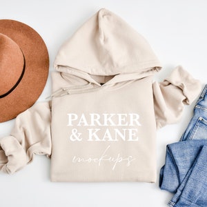May include: A beige hoodie with the text "Parker & Kane" in white lettering. The hoodie is laid flat on a white surface with a brown hat and blue jeans.