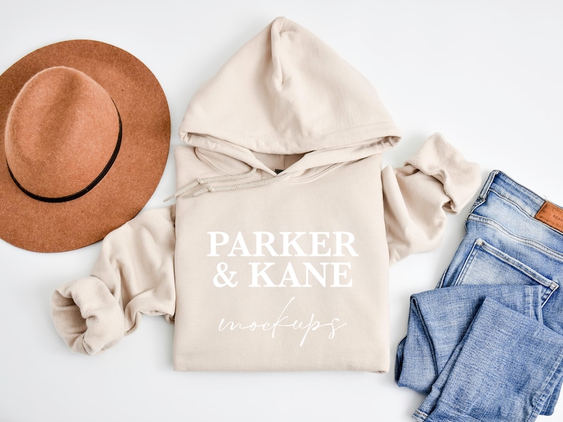May include: A beige hoodie with the text "Parker & Kane" in white lettering. The hoodie is laid flat on a white surface with a brown hat and blue jeans.