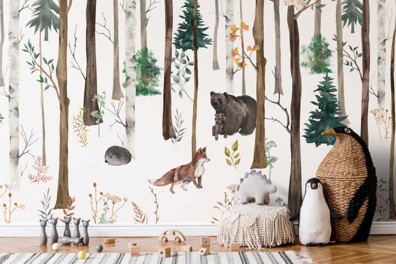 May include: A wall mural featuring a watercolor forest scene with birch and pine trees, a brown bear with a cub, a fox, and a hedgehog. In the foreground, there is a woven basket shaped like a penguin, a plush penguin, and a small dinosaur toy.