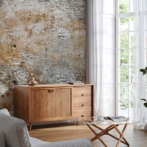 Puede incluir: Un aparador de madera con un panel de puerta tejido y dos cajones. El mueble est&aacute; colocado contra una pared texturizada con una mezcla de tonos grises, marrones y blancos. Tambi&eacute;n se ve una mesa de centro con tapa de cristal y cortinas blancas.