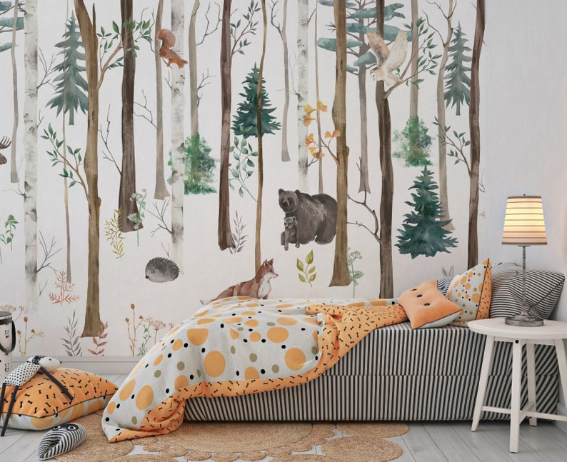 May include: A wall mural featuring a watercolor forest scene with birch and pine trees, a bear, a fox, a hedgehog, a squirrel, and an owl. The room includes a bed with a gray and white striped skirt, a patterned orange and gray quilt, and pillows.