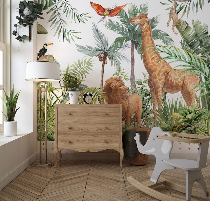 May include: A wall mural featuring a watercolor jungle scene with a giraffe, lion, monkey, toucan, and parrot amidst palm trees and foliage. A light wood three-drawer dresser, a floor lamp, and a gray elephant-shaped rocking chair are present.