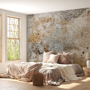 Puede incluir: Dormitorio con una cama en tonos neutros. La cama tiene almohadas, una manta de punto beige y una cesta de mimbre. Grandes ventanas y una pared texturizada completan la escena, creando un ambiente tranquilo.