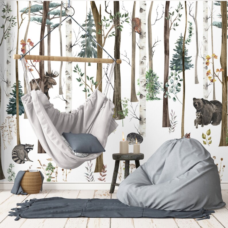 May include: A light gray hanging fabric swing chair with a dark gray pillow, a light gray bean bag chair, a small wooden stool with two candles, and a woven basket, set against a wall mural featuring a forest with birch trees and animals.