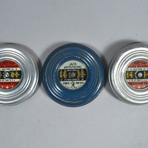May include: Three vintage pedometers. Two are silver-toned, labeled "Official Lone Ranger," and one is blue, labeled "Jack Armstrong." Each has a dial with stride measurements of 15, 20, and 25 inches. The pedometers are circular with a ridged edge.