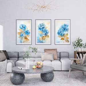Pode incluir: Três pinturas de aquarela emolduradas de hortênsias azuis com caules e folhas marrons em uma parede branca. As pinturas estão dispostas em fila, com a pintura do meio ligeiramente mais alta que as outras duas.