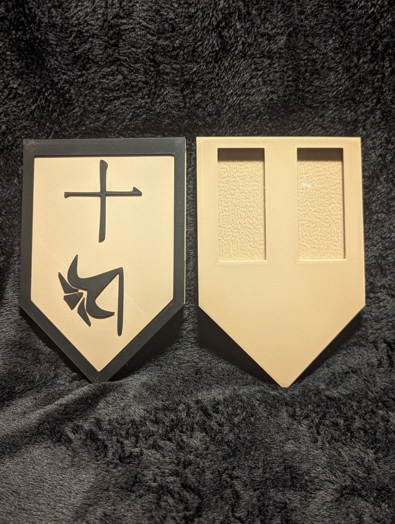 May include: Two wooden shields, one with a black border and a black and white symbol, the other with two empty slots. The symbol on the shield is a stylized cross with a stylized arrow pointing down.