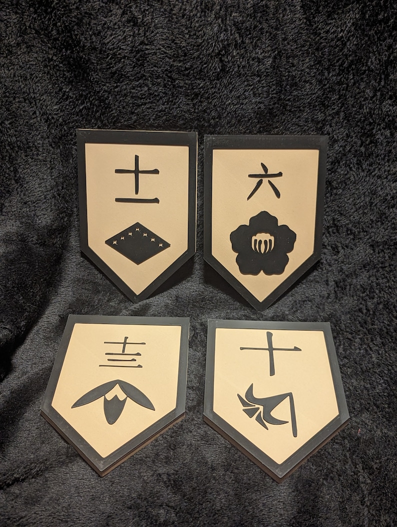 May include: Four beige and black shield-shaped plaques with Japanese characters and symbols. The plaques feature a flower, a cross, a geometric pattern, and a fan.
