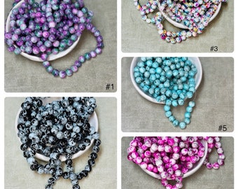 May include: Assortment of 10mm round glass beads with a speckled, marbled effect. The beads are available in five different color combinations: purple and green, white and multi-colored, black and white, pink and white, and blue and white.