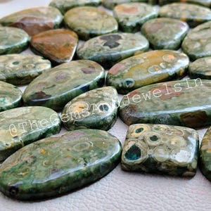 May include: A collection of green, brown, and white polished stones with a variety of patterns. The stones are oval and rectangular in shape. @TheGemsAndJewelsIn