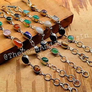 May include: A collection of nine silver bracelets with different colored gemstone beads. The bracelets feature a variety of stones, including carnelian, lapis lazuli, tiger's eye, and onyx. The bracelets are all made with a silver chain and a lobster clasp.