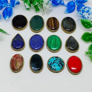 Può includere: Una collezione di dodici cabochon di pietre preziose in varie forme e colori, tra cui nero, verde, blu e rosso. Ogni pietra è incastonata in una cornice di metallo dorato con un design a corda ritorta.